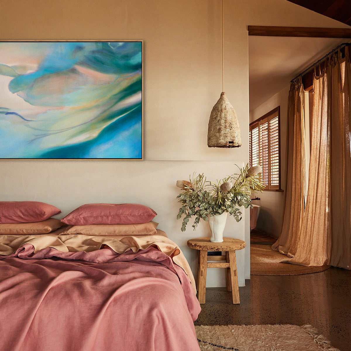 Bedroom with original abstract oil painting, pink bedding, and wooden stool with plants.