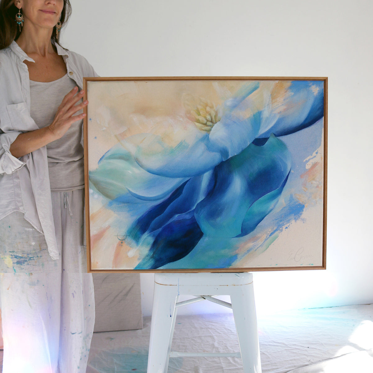 Woman holding a framed abstract painting with blue and beige colors.