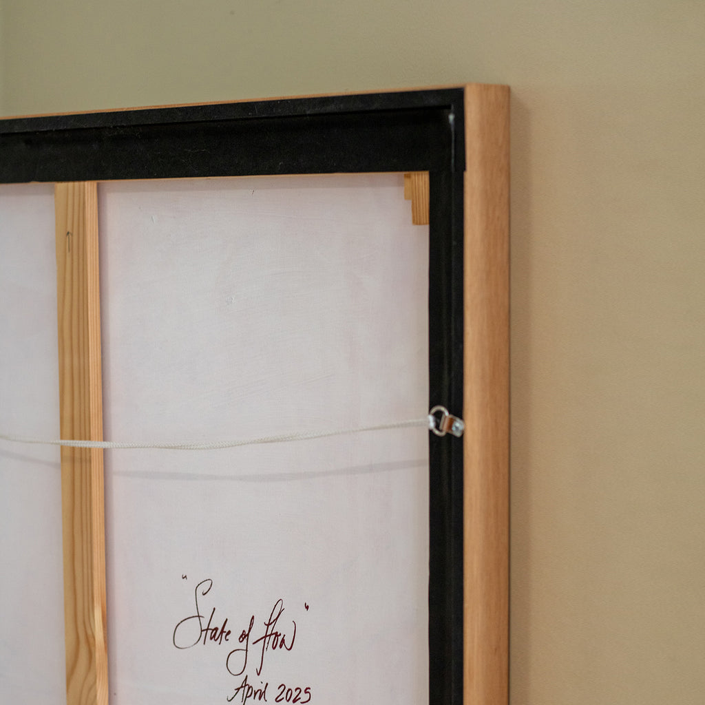 Framed artwork with a signature on a beige wall