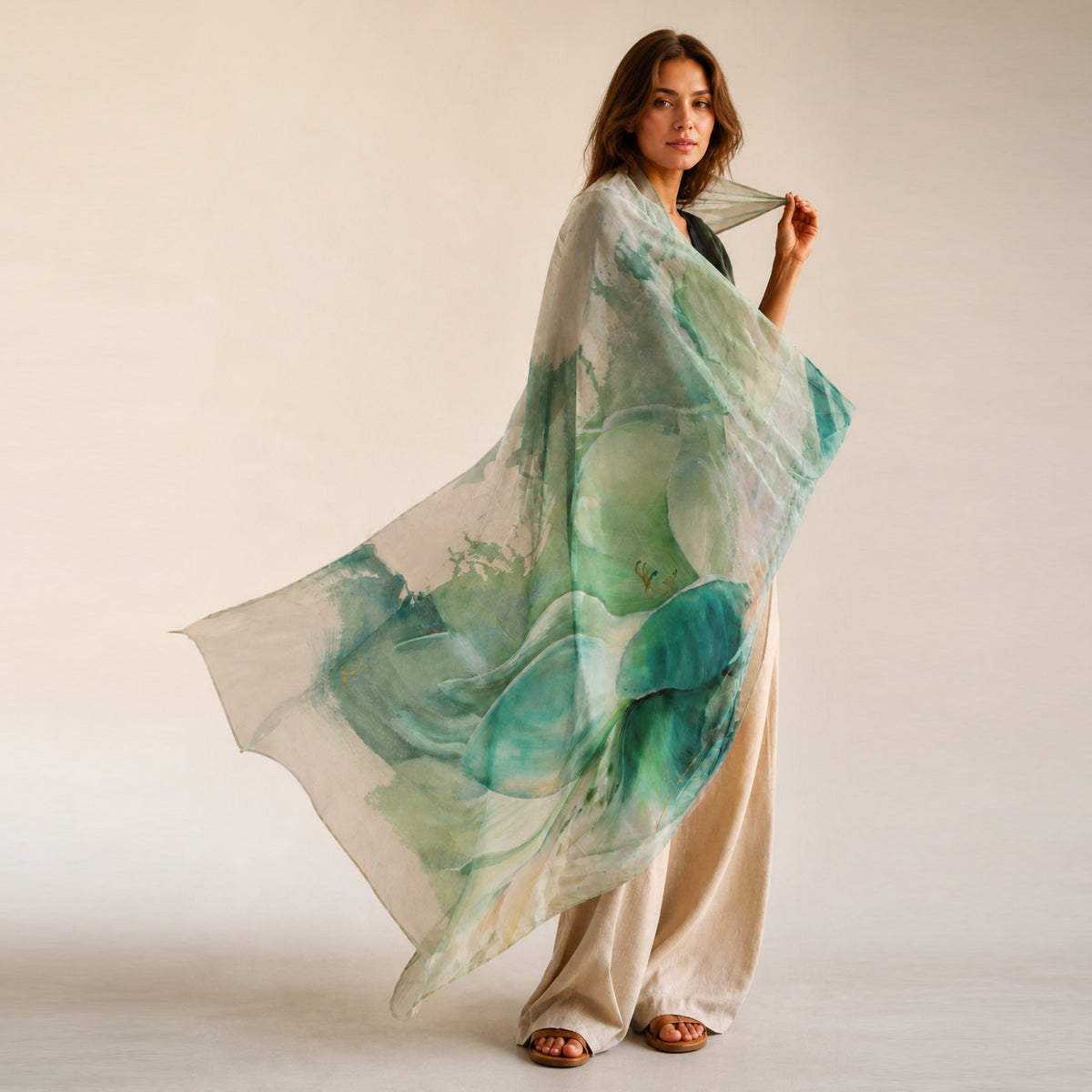 Woman holding a large green and white abstract floral scarf against a plain background